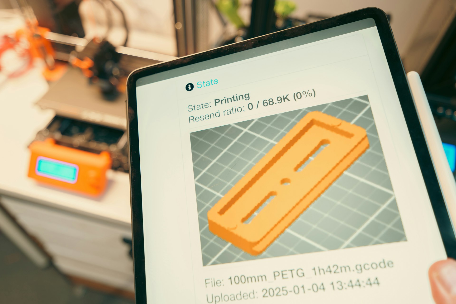Tablet displaying 3D print progress with printer in background.